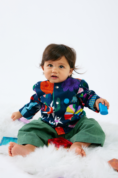 Baby wearing sustainable and colorful  baby clothes with a pattern of animals and plants on a white background