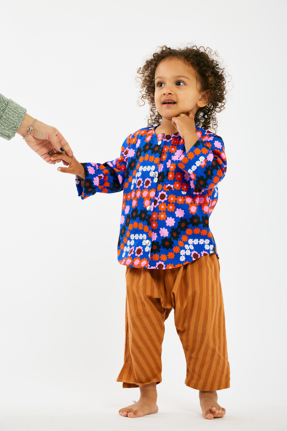 Child wearing a colorful patterned shirt and brown stripe pants on a white background