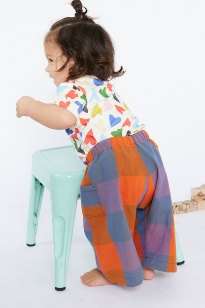 Child sitting on a mint green stool wearing colorful pants and a patterned shirt from Lilla Barn Clothing.