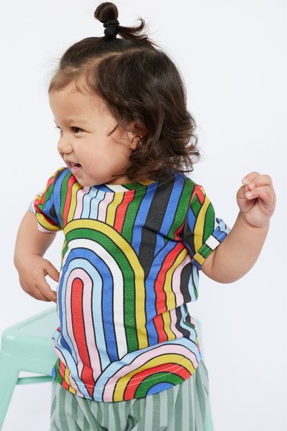 Child wearing a colorful striped shirt from Lilla Barn Clothing with a plain background