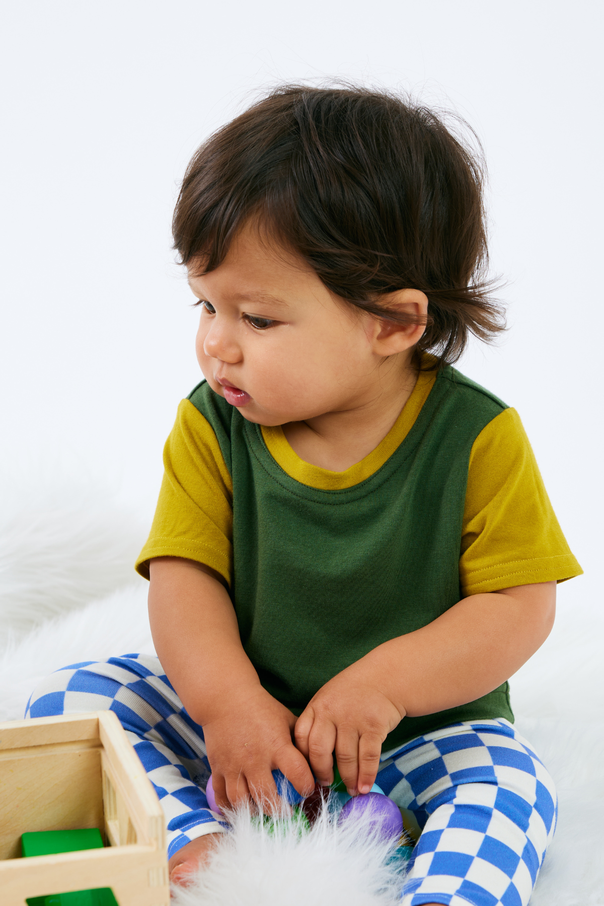 Baby wearing a green and yellow bamboo t-shirt with blue checkered organic cotton leggings, sitting on a white surface.