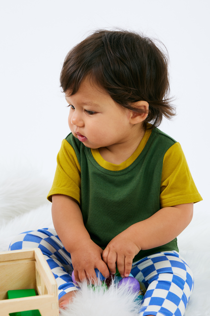 Baby wearing a green and yellow bamboo t-shirt with blue checkered organic cotton leggings, sitting on a white surface.