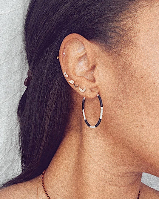 Close-up of an ear with hoop earrings and a necklace against a neutral background