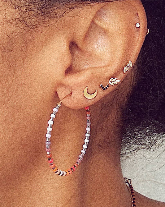 Close-up of an ear with multiple earrings including a beaded hoop earring.
