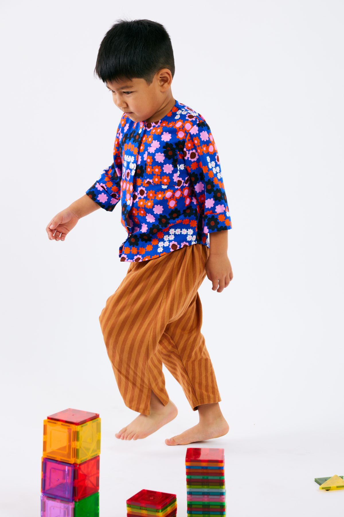 Child wearing a colorful kid top and orange stripe pants while playing with colorful blocks on a white background