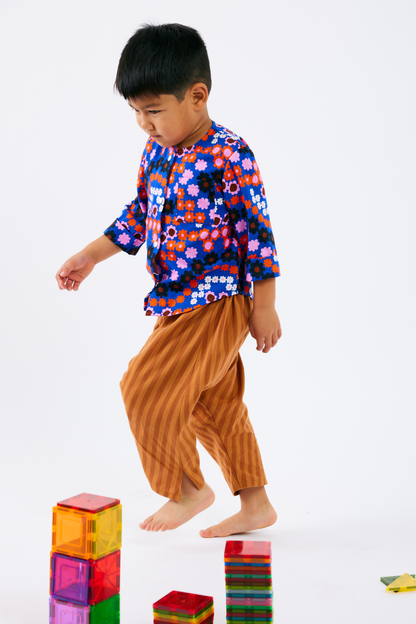 Child wearing a colorful kid top and orange stripe pants while playing with colorful blocks on a white background