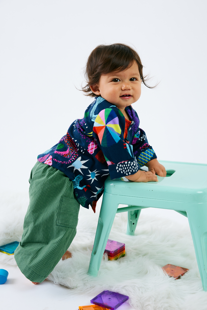 Baby wearing sustainable and colorful  baby clothes with a pattern of animals and plants on a white background
