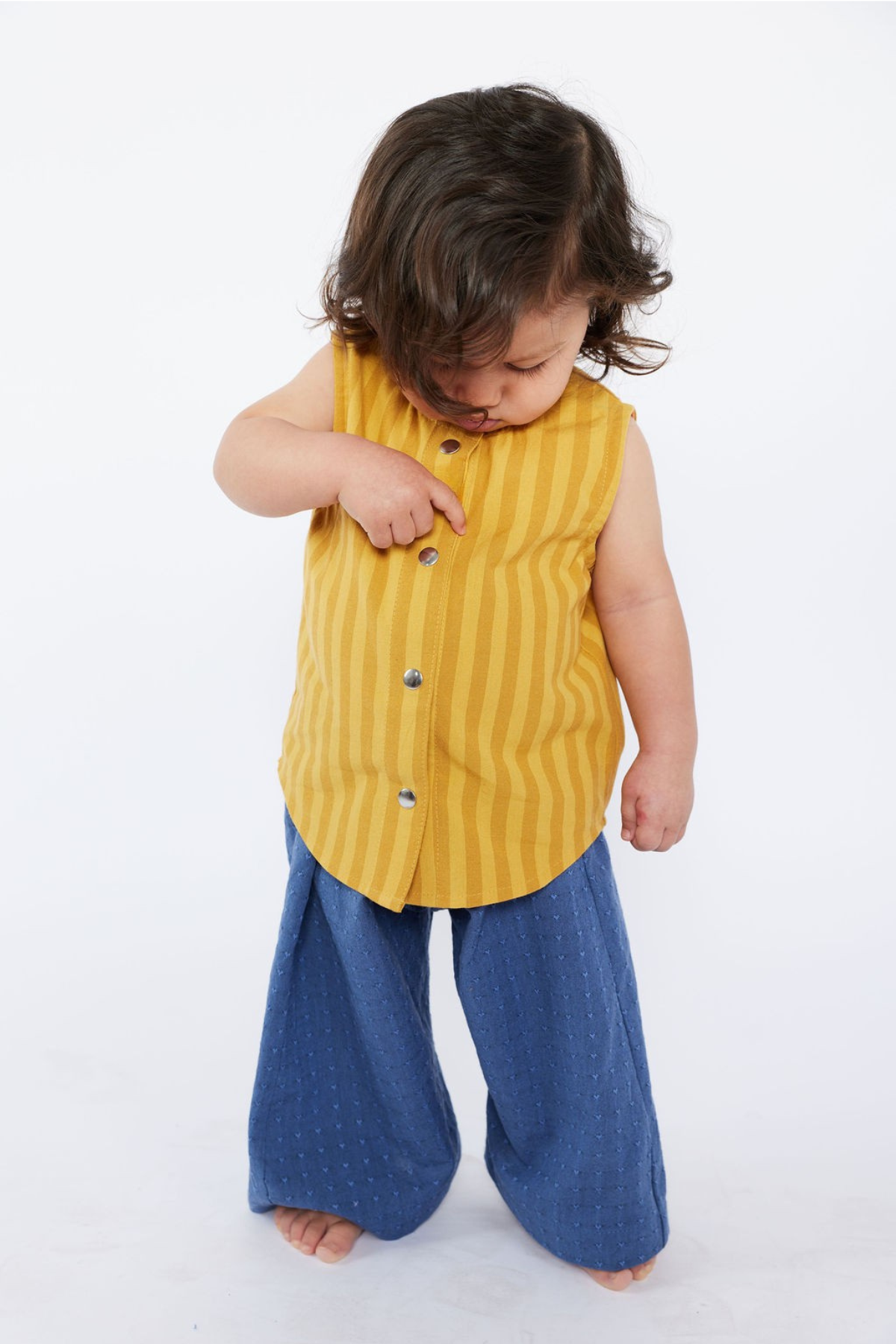 Child wearing a yellow sleeveless shirt with buttons and blue pants on a white background