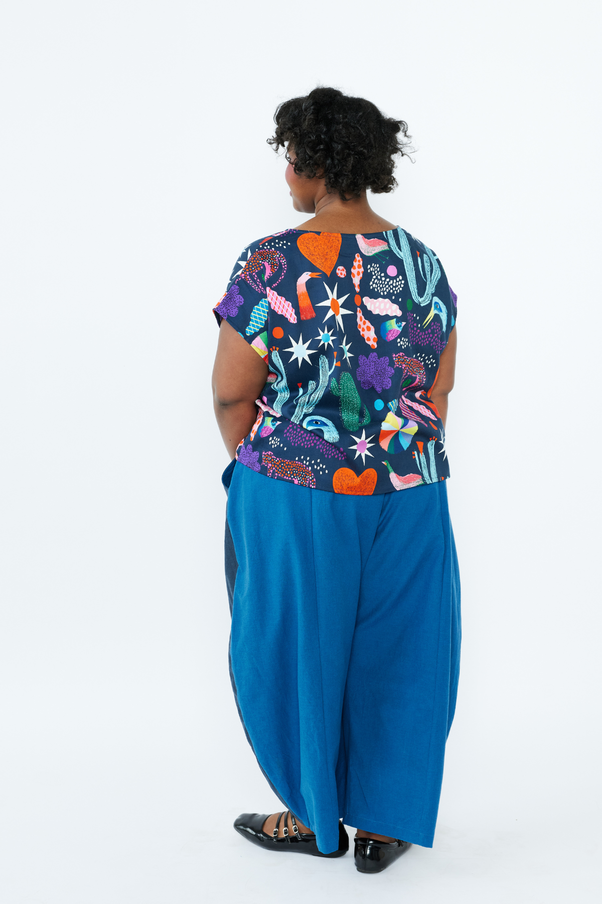 Person wearing a colorful patterned top and blue pants on a white background