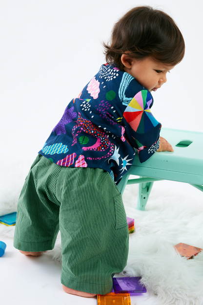 Child wearing a colorful shirt and green striped pants playing with colorful toys on a white surface