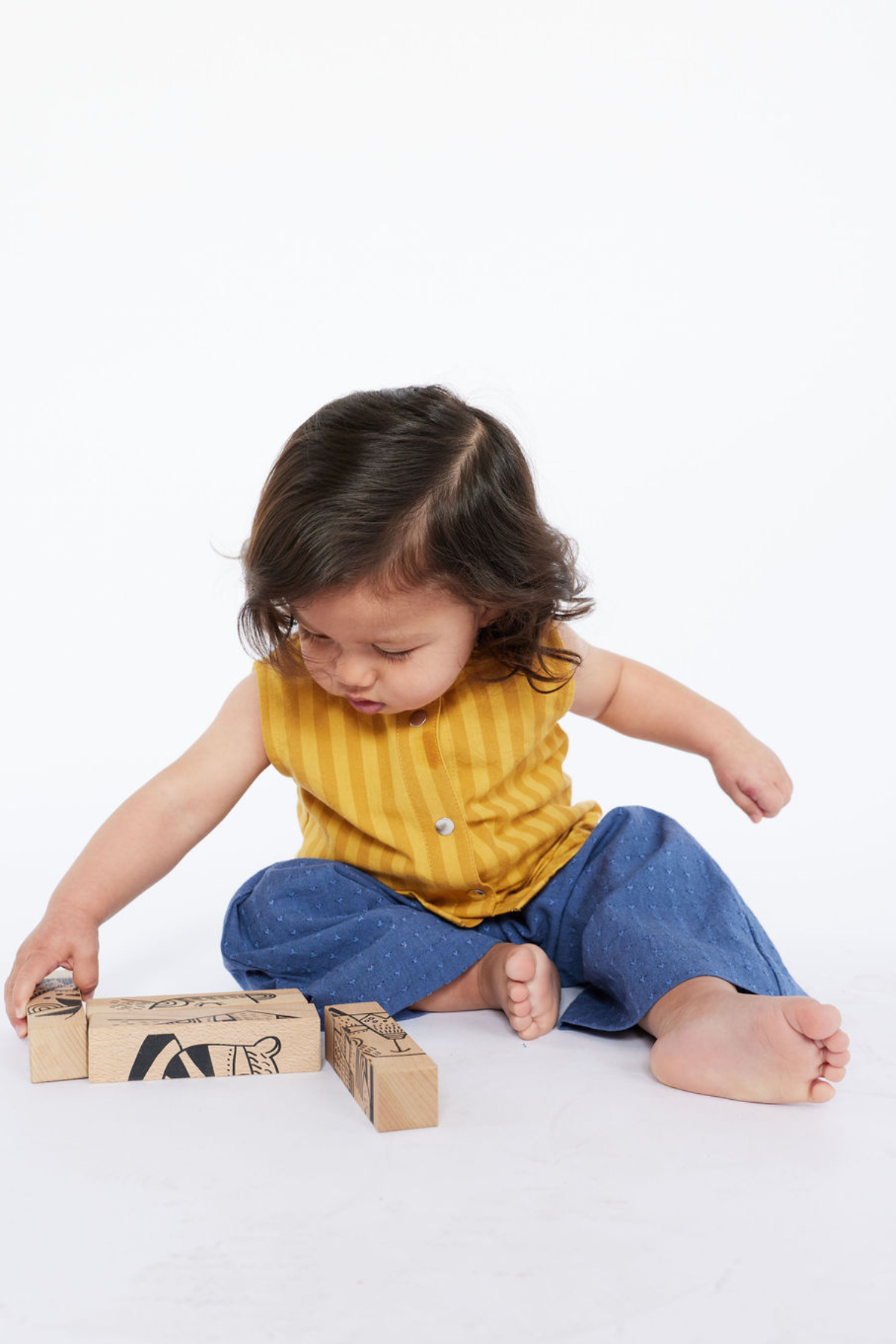 Child playing with blocks wearing a yellow stripe tank and blue pants on a white background