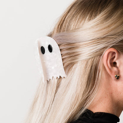 Person wearing a white ghost-shaped hair clip on a plain background