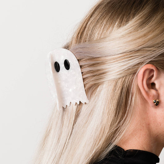 Person wearing a white ghost-shaped hair clip on a plain background