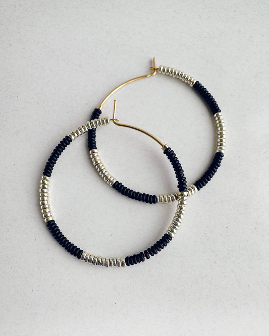 Pair of beaded hoop earrings with black and silver beads and 14k gold fill wires on a light gray background
