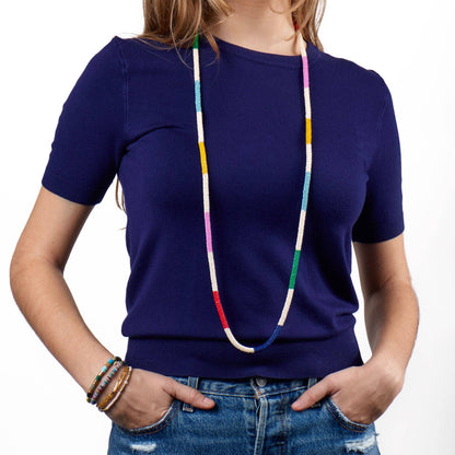 Person wearing a blue shirt with a colorful beaded necklace on a white background