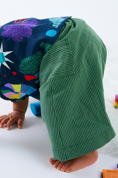 Child wearing cotton green stripe pants with a colorful shirt, standing on a white surface.