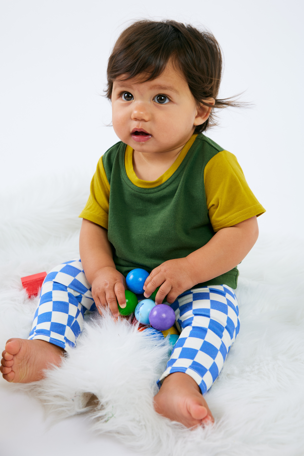 Baby wearing a green and yellow bamboo t-shirt with blue checkered organic cotton leggings, sitting on a white surface.