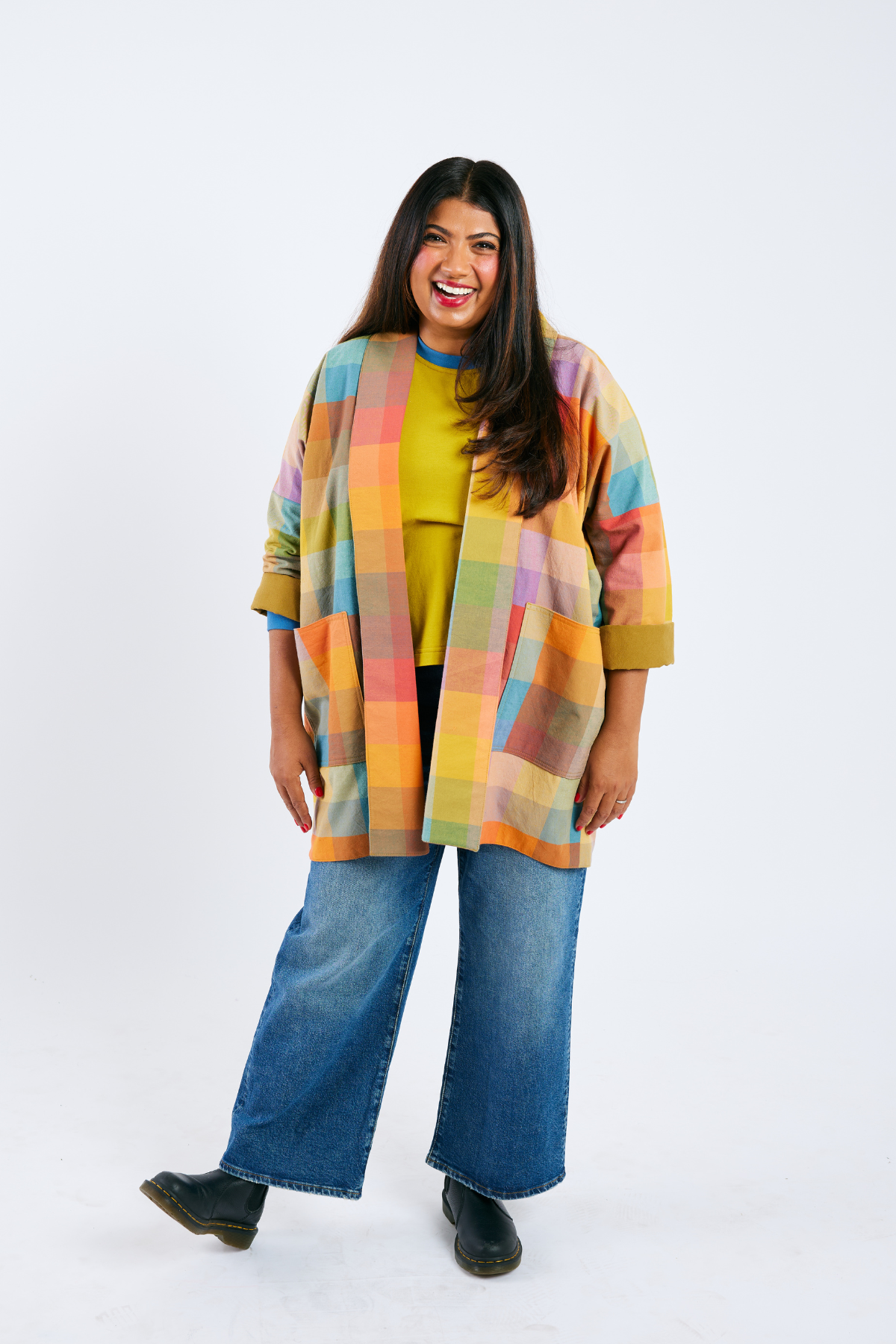 Woman wearing a colorful plaid jacket over a yellow top and blue jeans on a white background