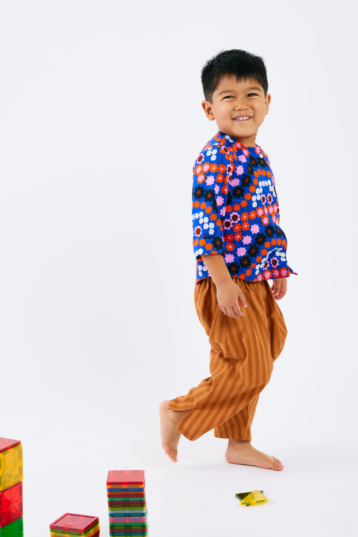 Child wearing a colorful shirt and brown pants with building blocks on a white background