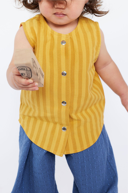 Child wearing a yellow striped shirt and blue pants holding a wooden block.