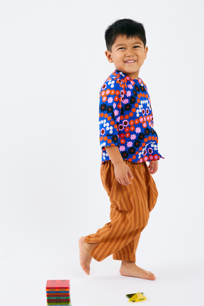 Child wearing a colorful floral shirt and brown pants on a white background