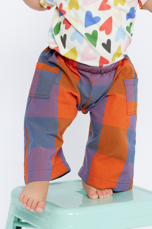 Child wearing colorful checkered pants and a shirt with heart patterns on a white background