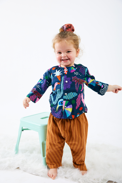 Child wearing a colorful kid shirt with abstract patterns and brown striped pants on a white background