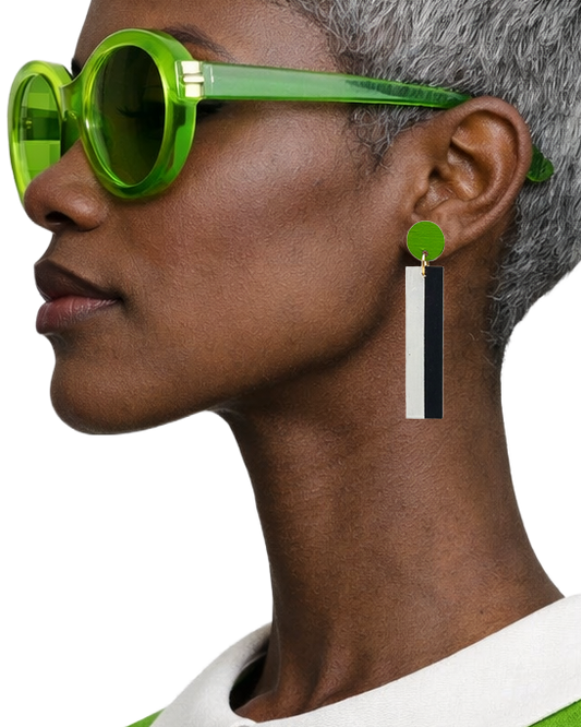 A close-up side profile of a model with short gray hair wearing bright green sunglasses and a matching green-and-white top, highlighting a dangling statement earring with a green top, white rectangular drop, and black center stripe.