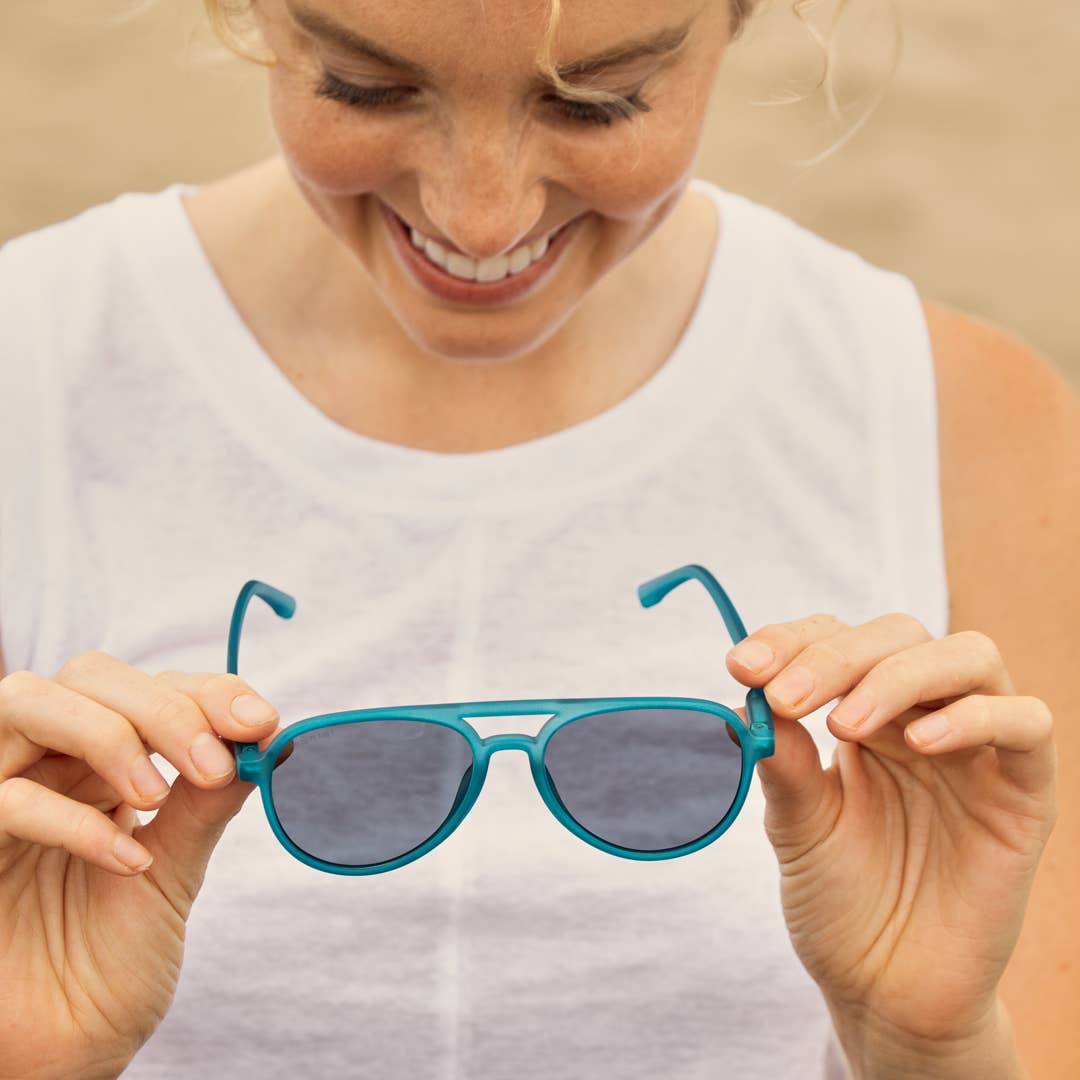 Woman holding a pair of blue sunglasses against a beige background