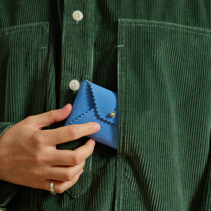 Hand holding a blue wallet against a green corduroy shirt background