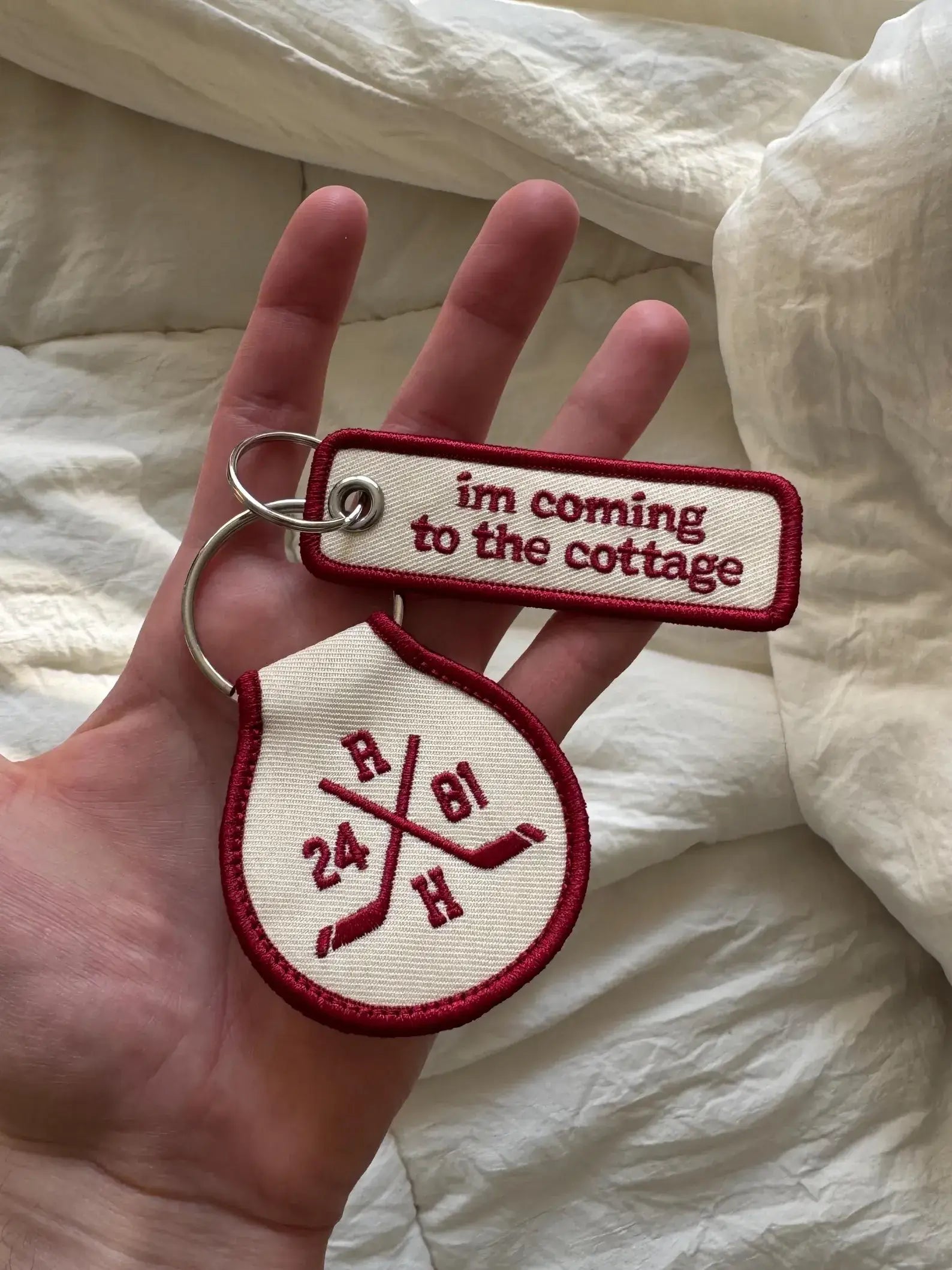 Two keychains held in a hand with text and symbols on a white fabric background
