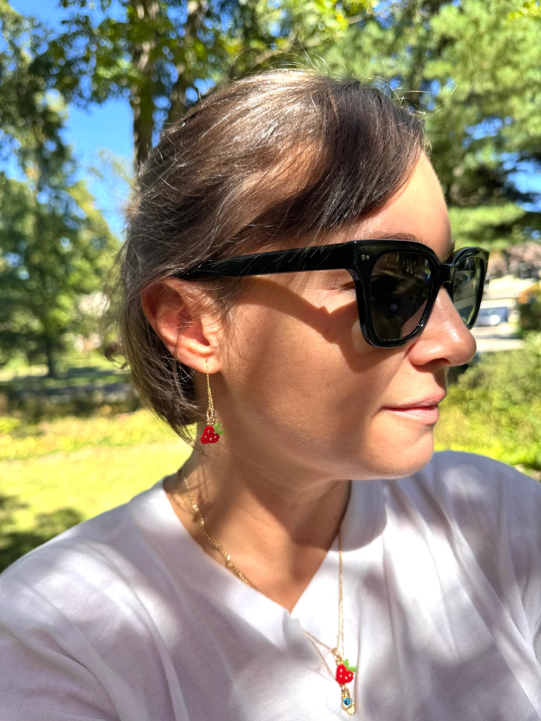 person in a park wearing red strawberry woven bead ear threader earrings on 14k gold filled wire