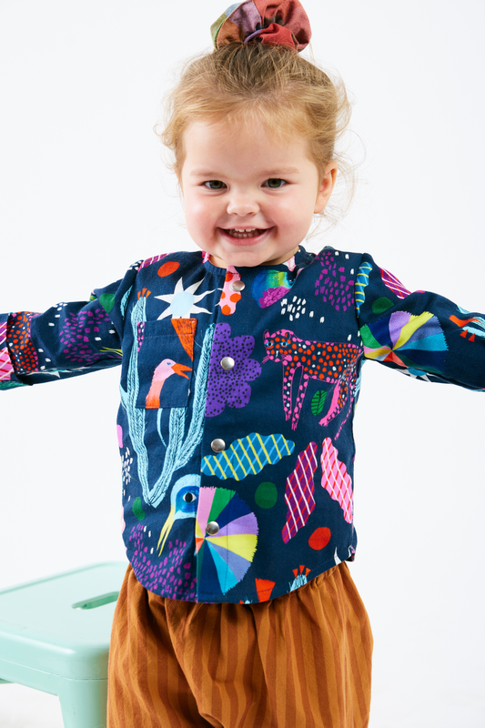 Child wearing a colorful kid shirt with abstract patterns and brown striped pants on a white background
