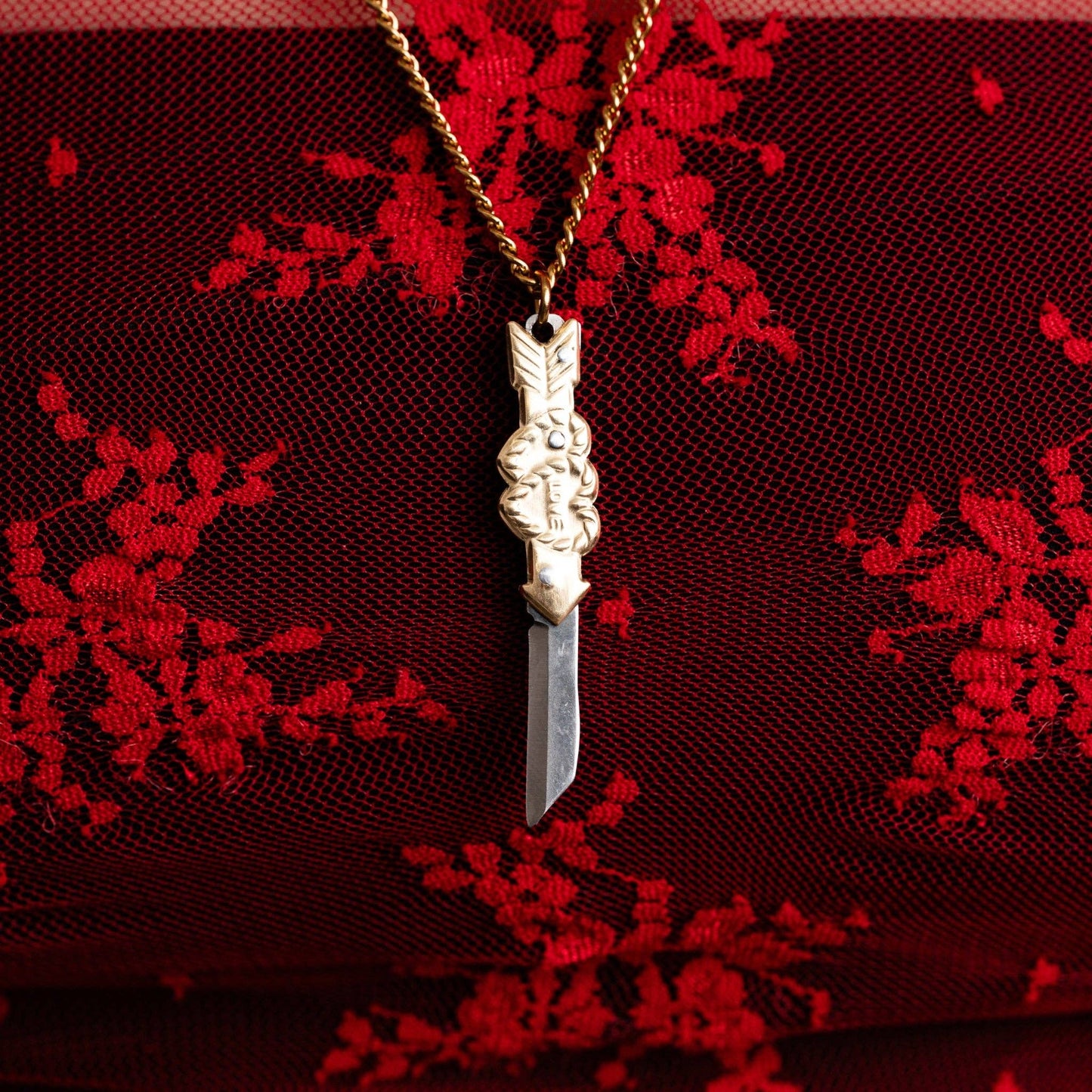 Decorative switchblade pendant necklace on a red textured fabric background