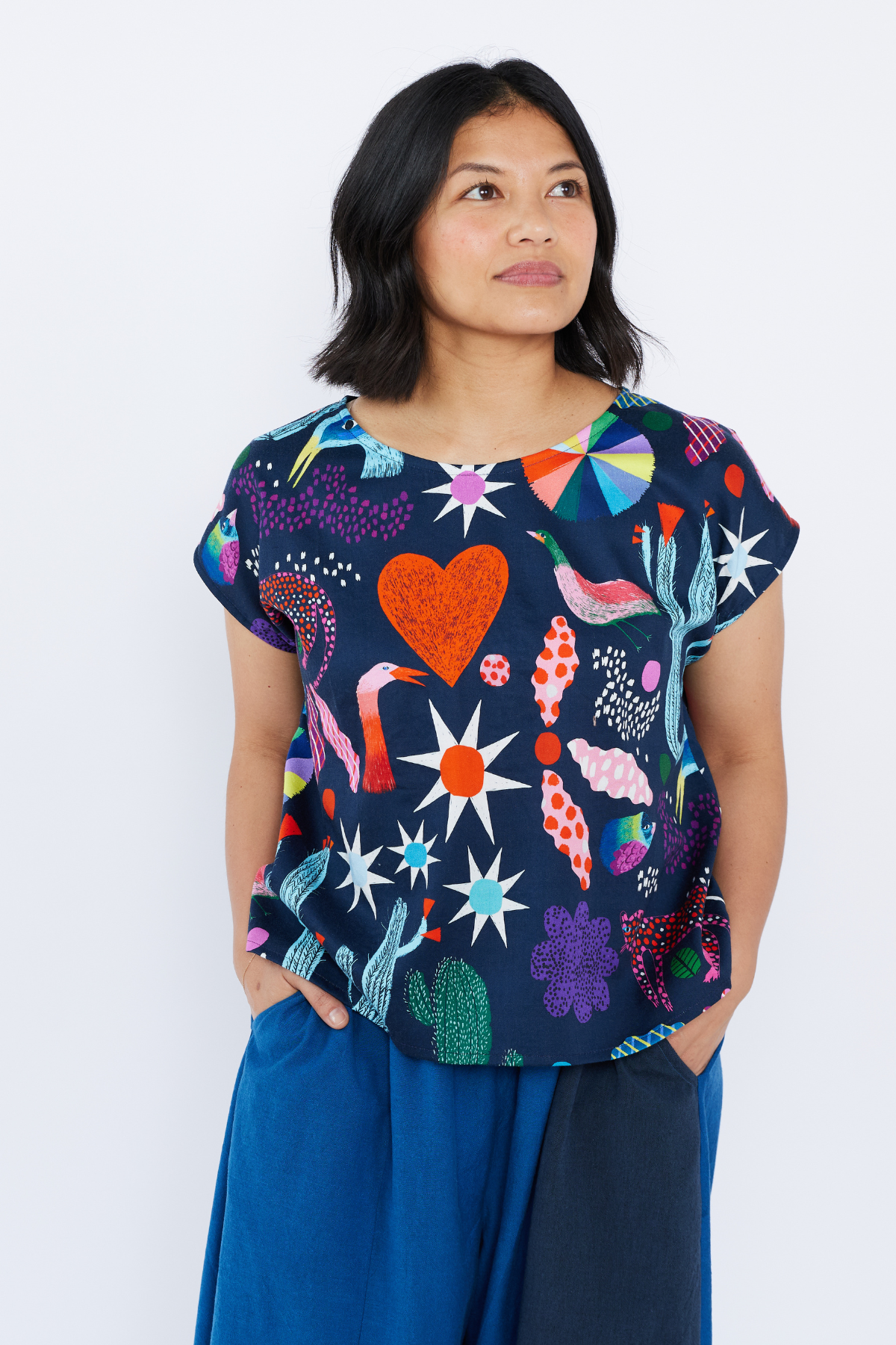Woman wearing a colorful patterned top with blue pants on a white background