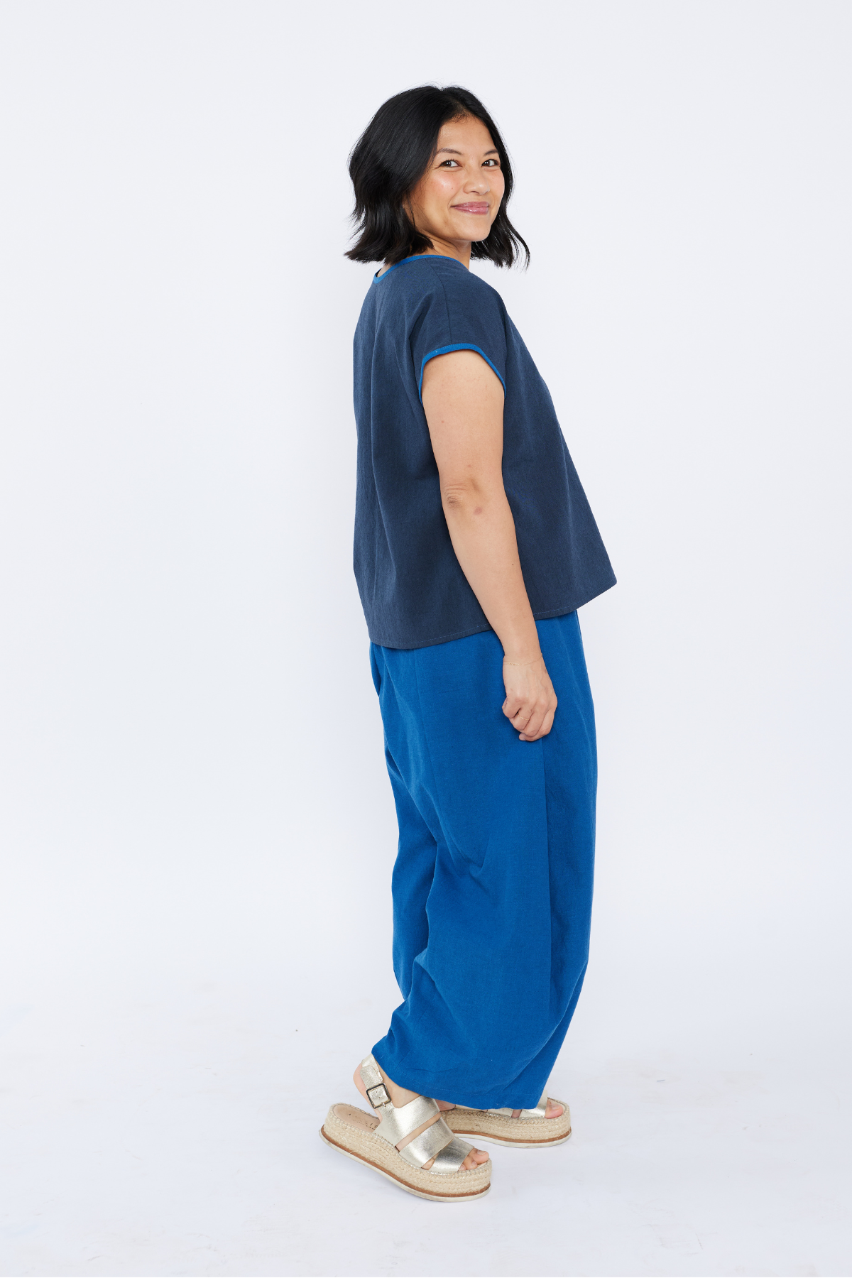 Woman wearing a navy top and blue pants on a white background