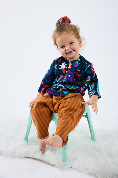 Child sitting on a chair wearing a colorful blue shirt and brown pants against a white background
