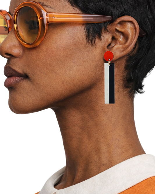 A close-up side profile of a model wearing a long dangle earring. The earring features a bright red circular top, a gold-tone connector, and a vertical rectangular drop split into a white top half and a black bottom half.