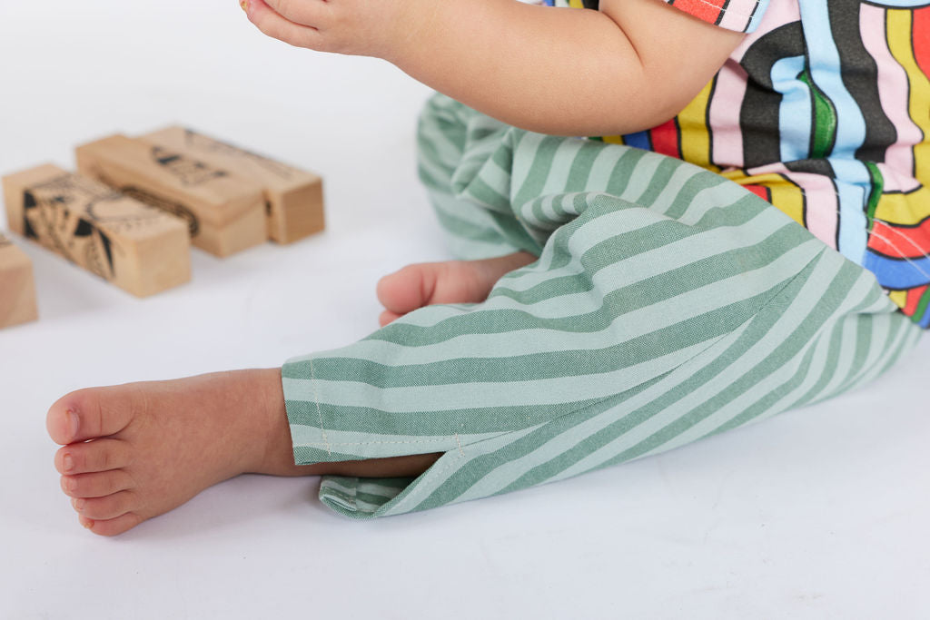 Child's legs wearing green striped pants on a white surface with wooden blocks.