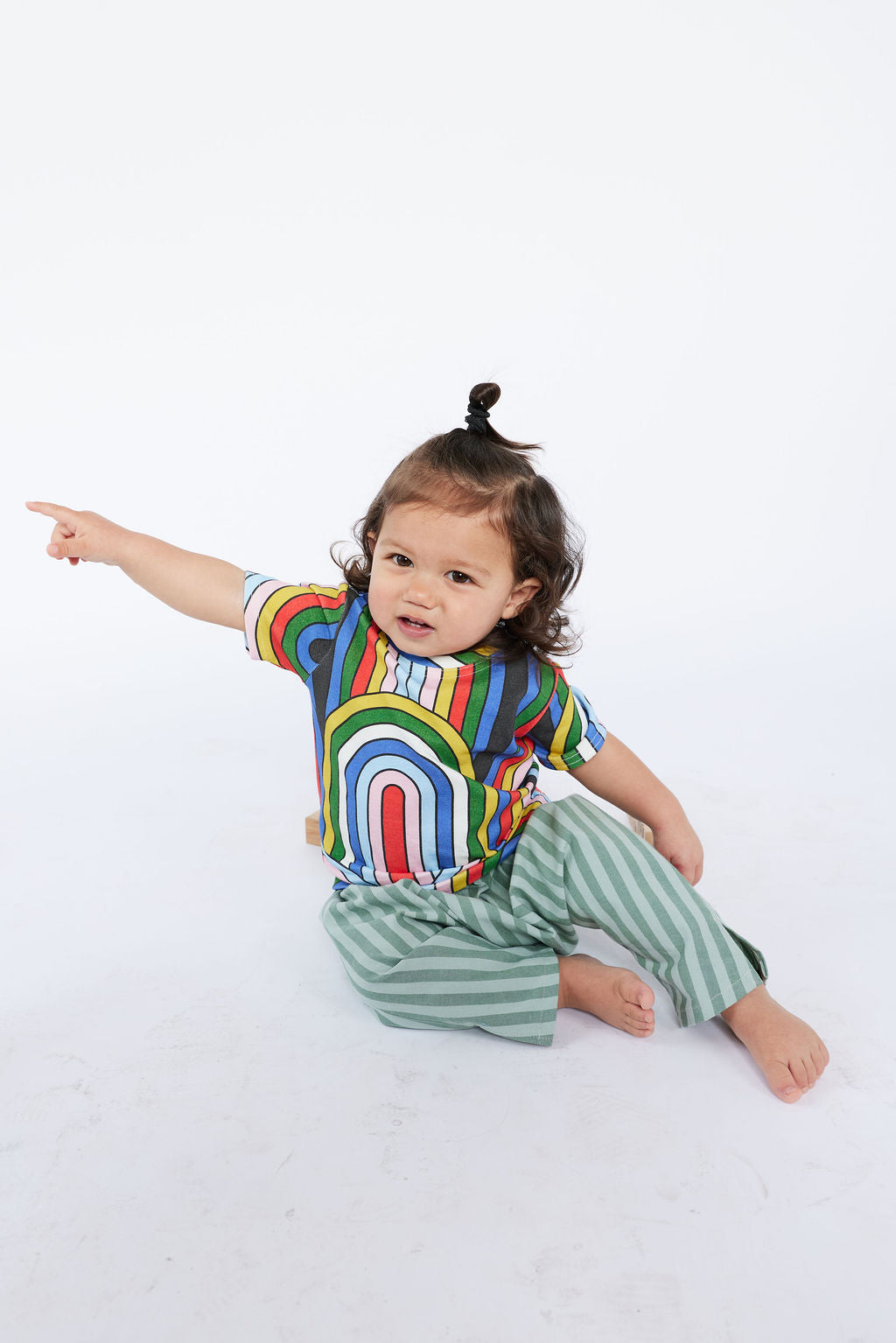 Child wearing a colorful rainbow shirt and green striped pants on a white background