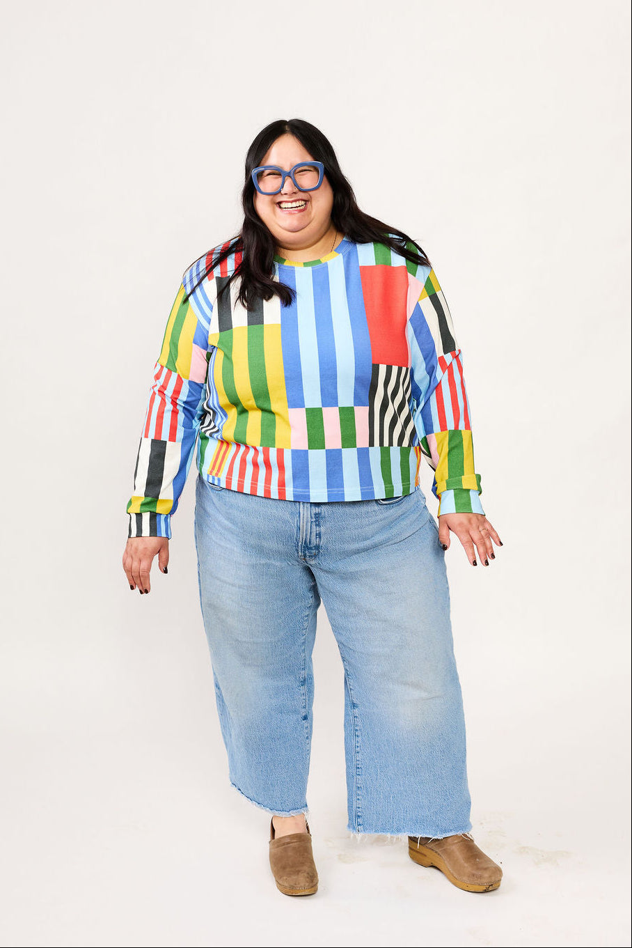 Person wearing a colorful striped Lilla Barn shirt and jeans on a white background
