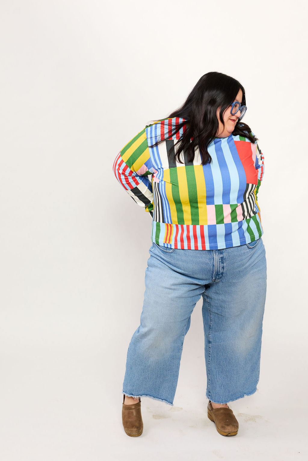 Person wearing a colorful striped shirt from Lilla Barn and blue jeans on a white background