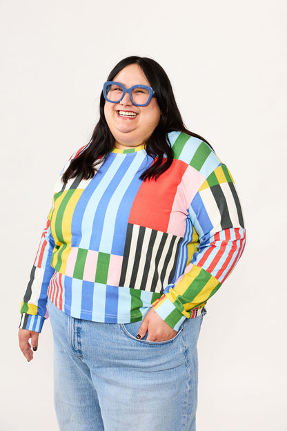 Person wearing a colorful Window Stripe shirt from Lilla Barn Clothing and blue jeans on a white background