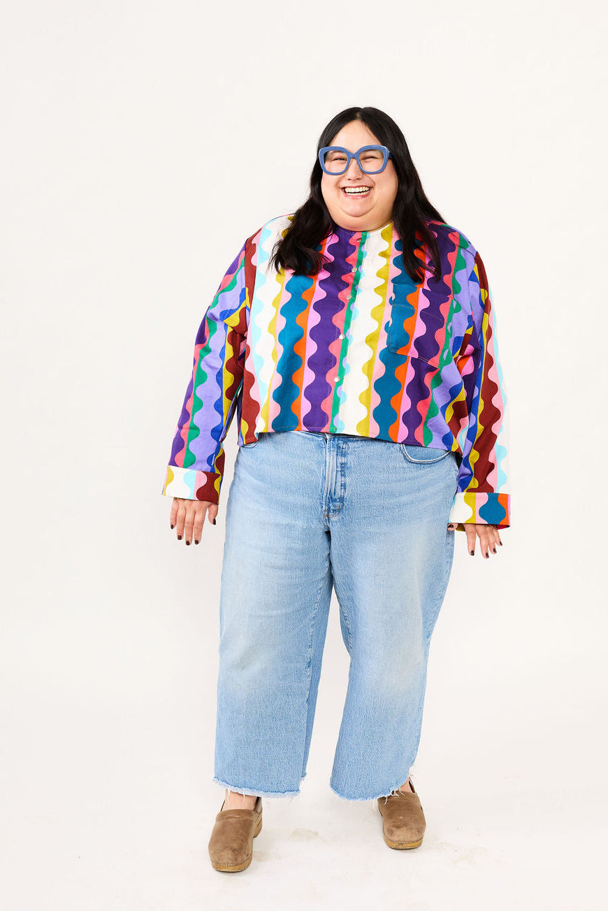 Person wearing a colorful Lilla Barn Clothing shirt and light blue jeans on a white background