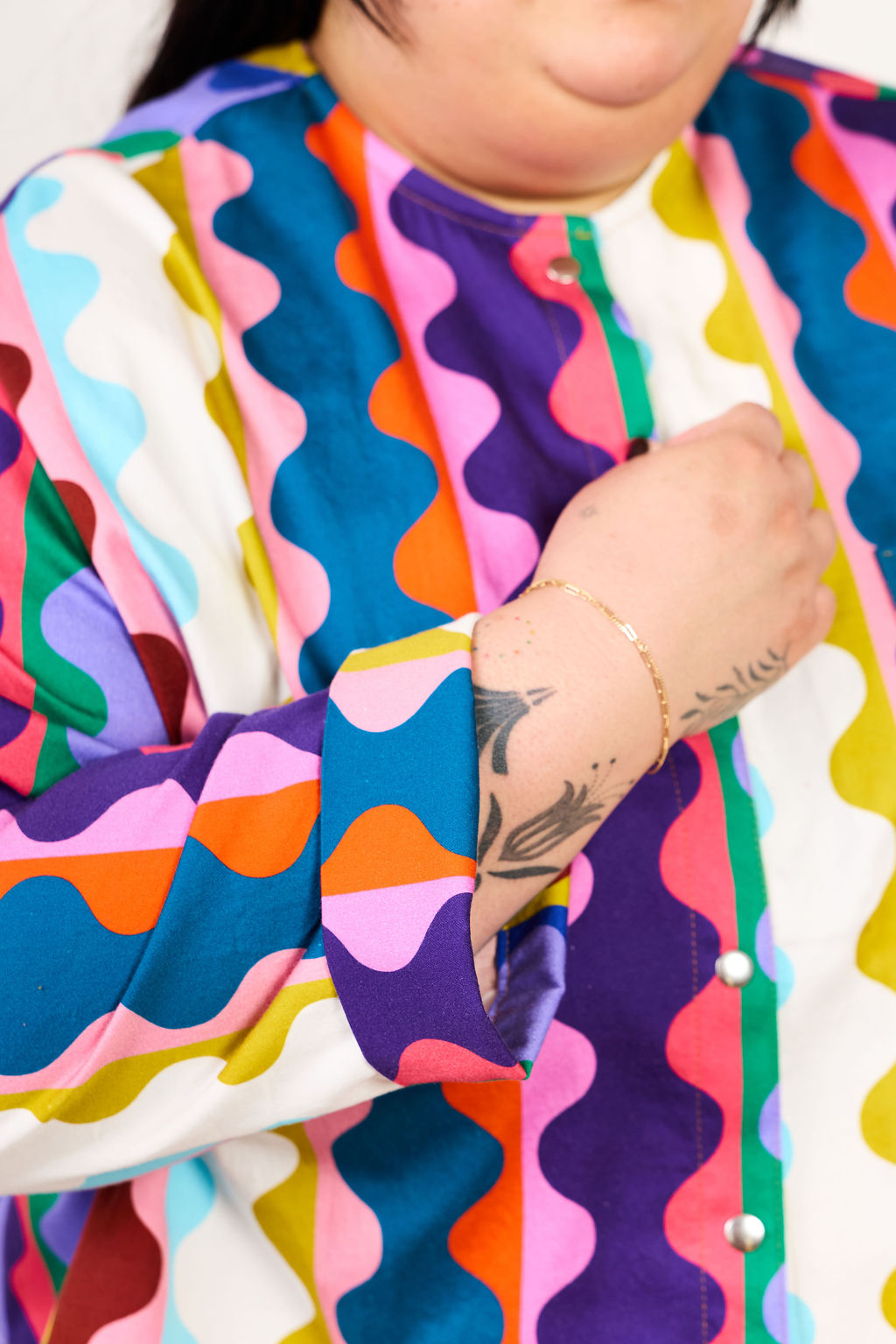 Person wearing a colorful, patterned jacket with tattoos visible on arms.