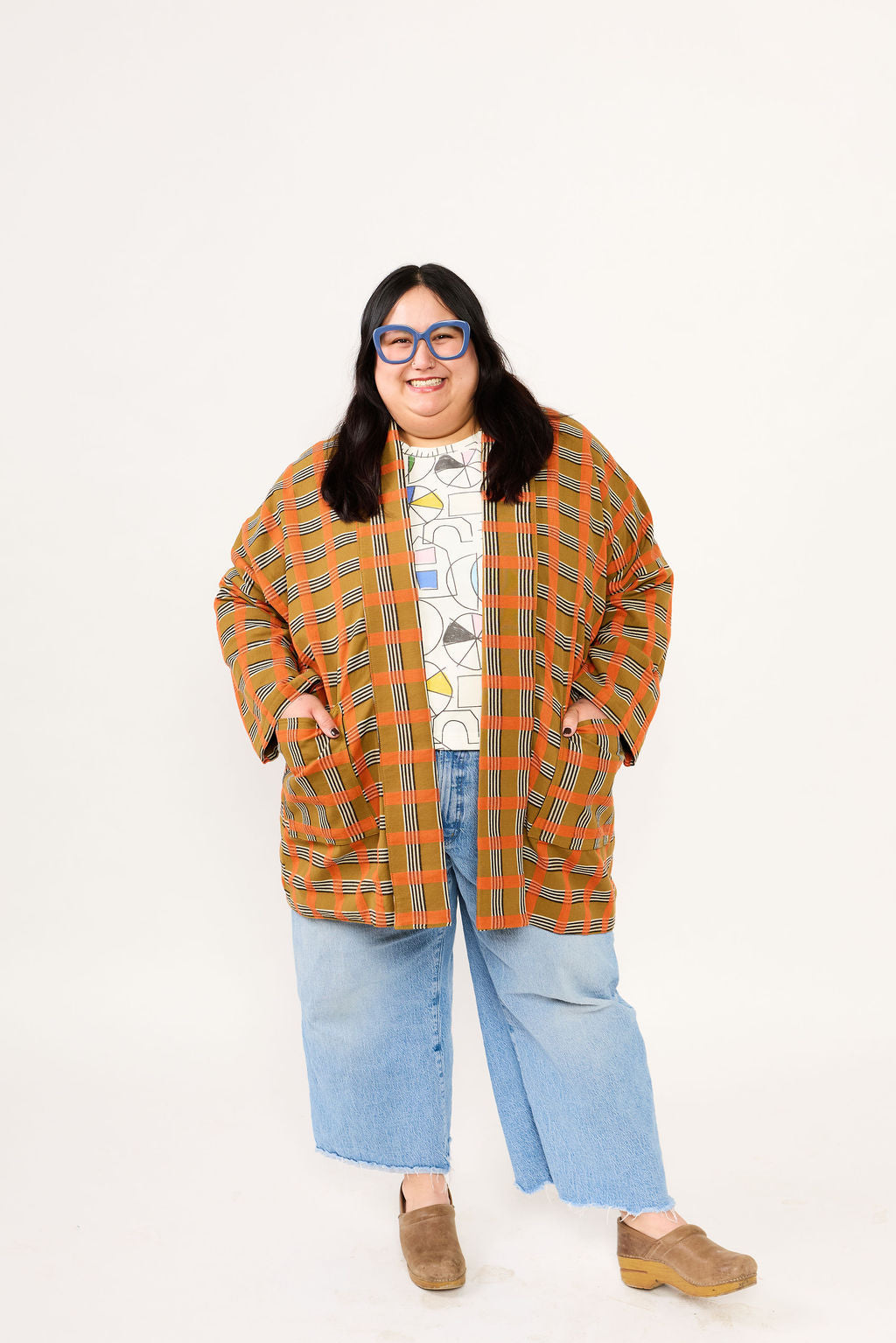 Person wearing a plaid orange and green coat with a white background