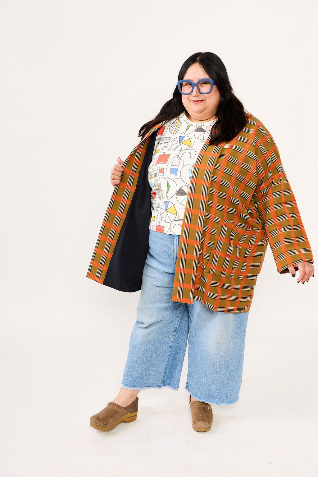 Person wearing a colorful plaid jacket over a patterned shirt with light blue jeans on a white background