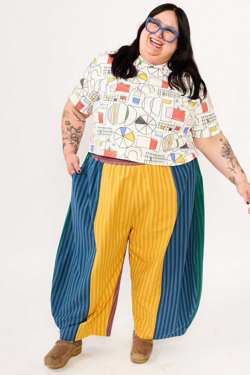 Person wearing a colorful patterned shirt and multicolored pants on a white background