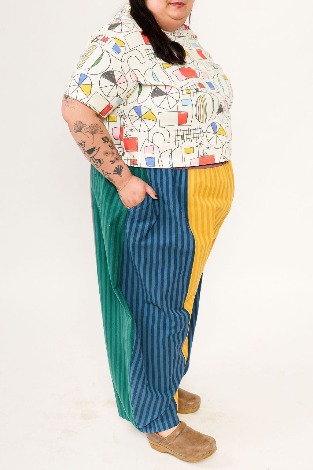 Person wearing a colorful geometric-patterned shirt and multicolored pants on a white background