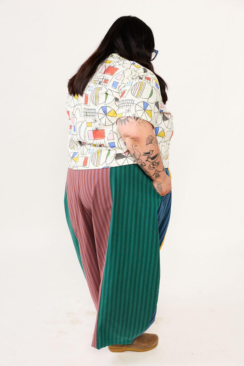 Person wearing a colorful patterned top and long pants on a white background